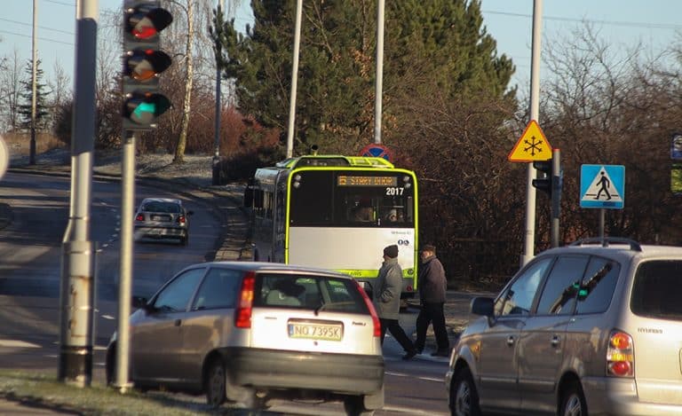 Autobus i samochody na skrzyżowaniu w Olsztynie, widoczne światła i znaki drogowe.
