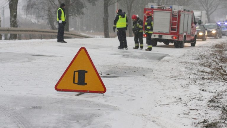 Straż pożarna i policja na miejscu kolizji autobusu w Kieźlinach, w tle śnieg i zablokowana droga.