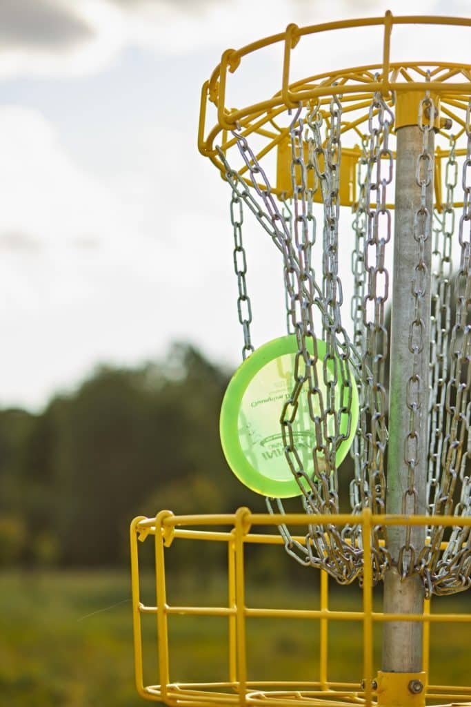 Dysk golfowy w koszu na pełnowymiarowym polu na zewnątrz, z chmurami w tle.