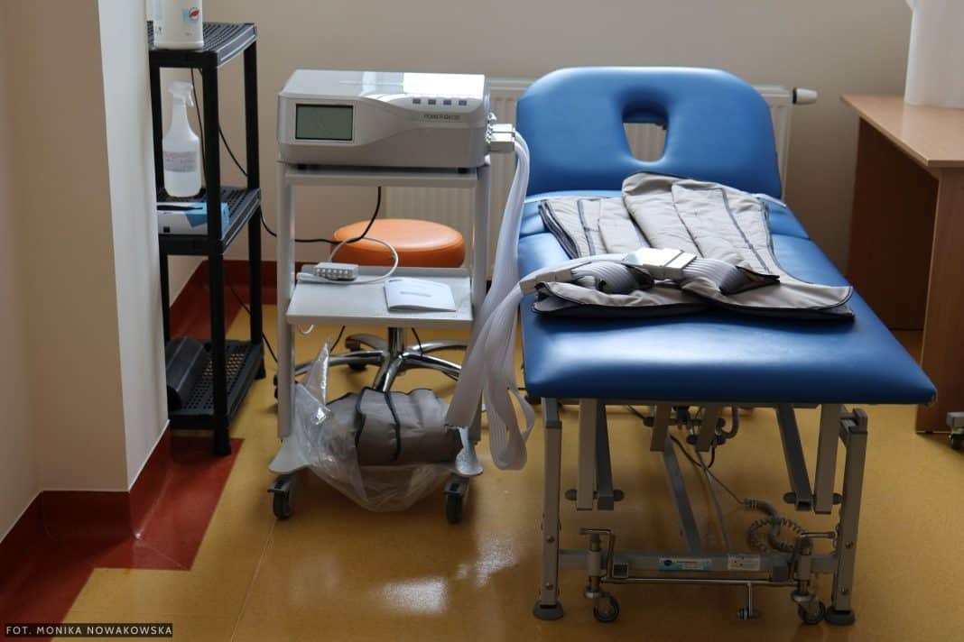 Wyposażenie sali rehabilitacyjnej z ł&oacute;żkiem, urządzeniami medycznymi i akcesoriami.