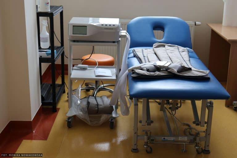 Wyposażenie sali rehabilitacyjnej z ł&oacute;żkiem, urządzeniami medycznymi i akcesoriami.