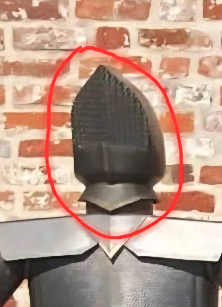 Zniszczona figura rycerza z odciętą głową, zaznaczona czerwoną linią, na tle ceglanej ściany.