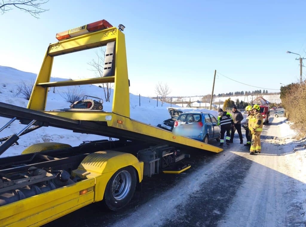 Zdjęcie przedstawia samoch&oacute;d lawetę na drodze, obok rozbite dwa pojazdy i służby ratunkowe.
