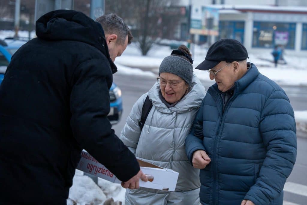 Prezydent Olsztyna rozdaje pączki mieszkańcom na ulicy w zimowej scenerii.