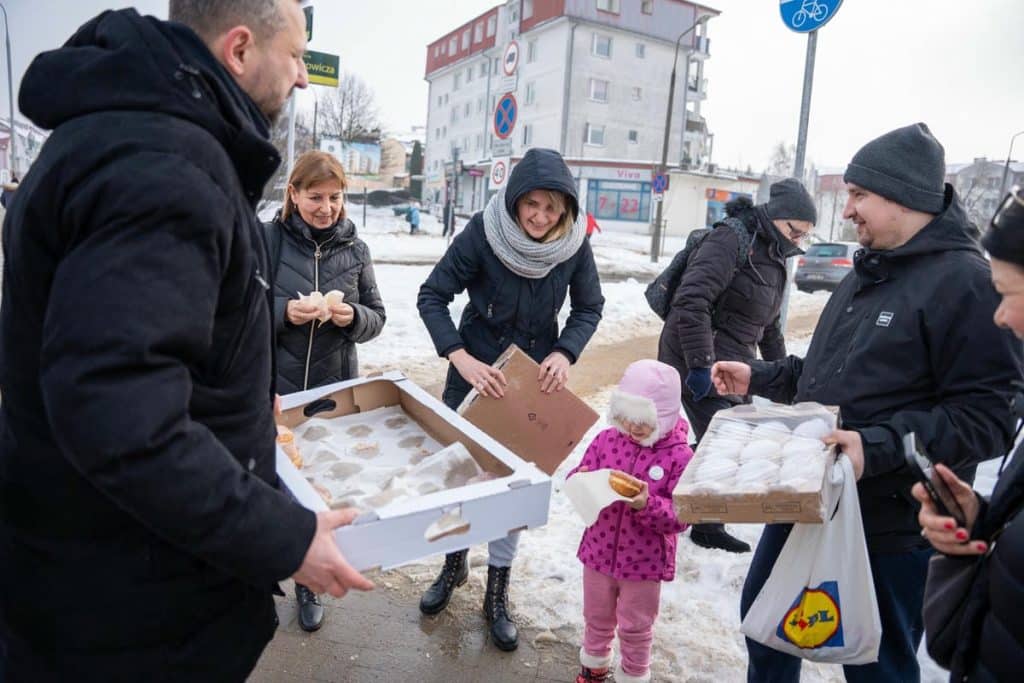 Prezydent Olsztyna rozdaje pączki mieszkańcom na ulicy w zimowej scenerii.