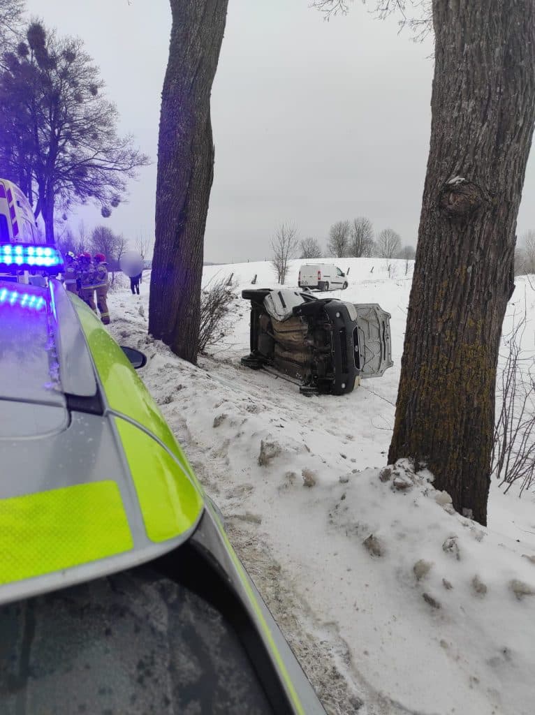 Samoch&oacute;d po uderzeniu w drzewo na drodze wojew&oacute;dzkiej, widok na miejsce zdarzenia z służbami ratunkowymi.