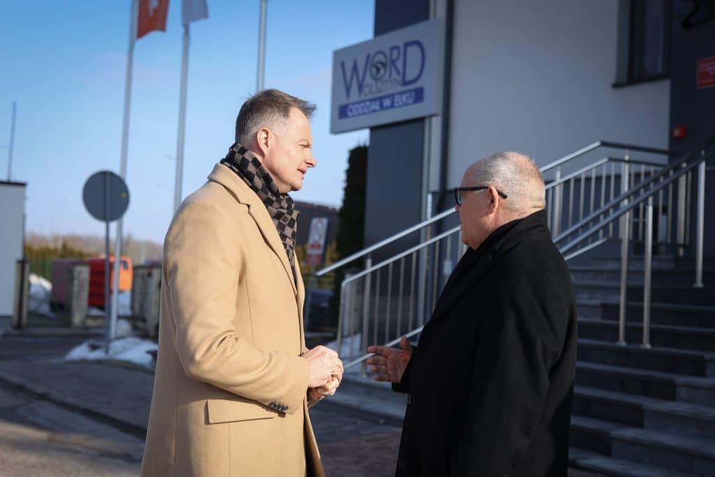 Dw&oacute;ch mężczyzn rozmawia przed budynkiem WORD w Ełku, na zewnątrz, w słoneczny dzień.