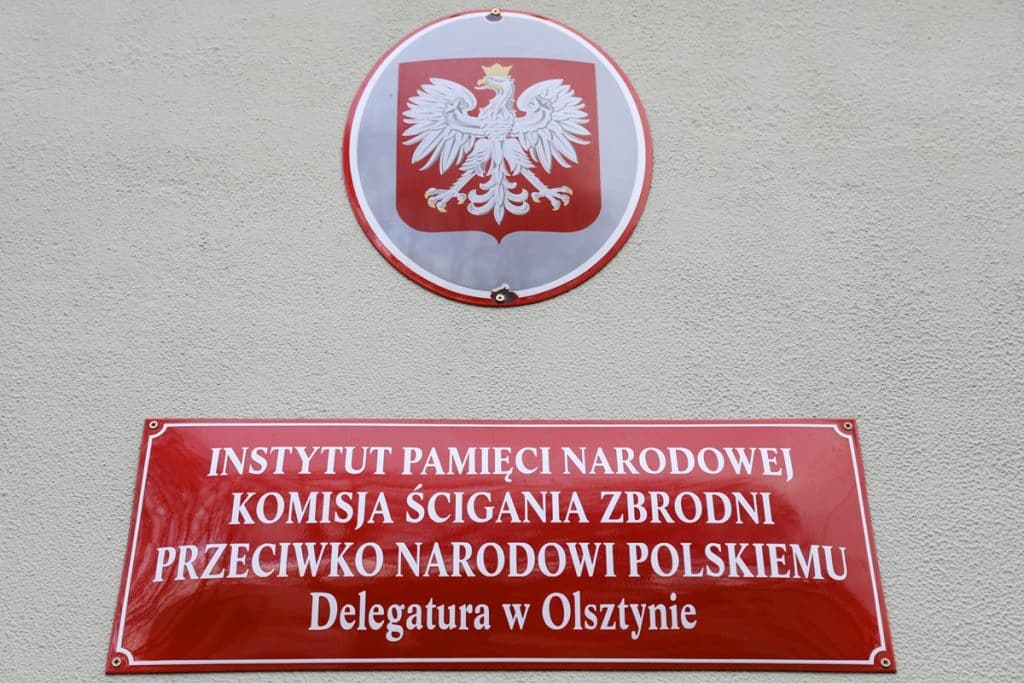 Tablica informacyjna na ścianie budynku IPN w Olsztynie, z godłem Polski i napisem o nowej siedzibie delegatury.