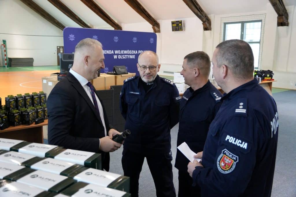 Policjanci rozmawiają podczas wydarzenia w sali sportowej, w tle sprzęt i materiały szkoleniowe.