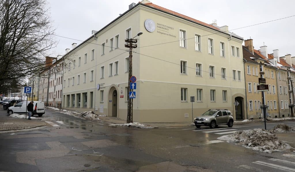 Nowa siedziba Delegatury IPN w Olsztynie na tle miejskiej ulicy, zimowa pogoda, śnieg i mokra nawierzchnia.