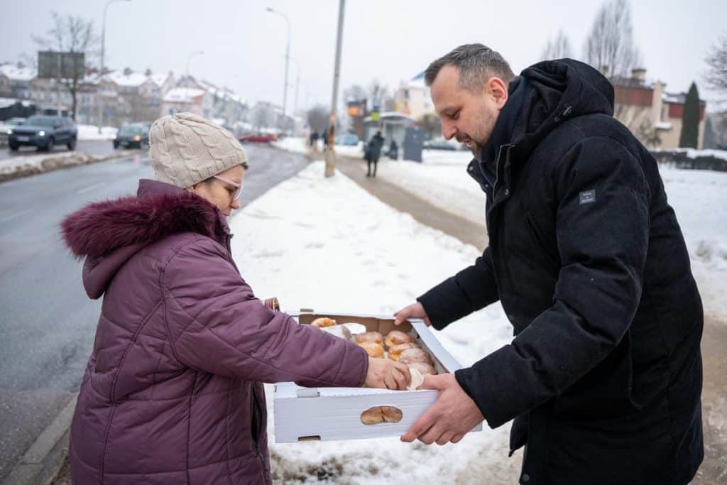 Prezydent Olsztyna rozdaje pączki mieszkańcom na ulicy w zimowej scenerii.