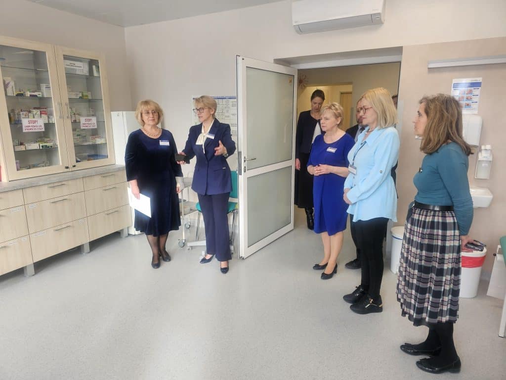 Grupa os&oacute;b w szpitalu dziecięcym podczas wizyty lub inspekcji, w tle nowoczesne pomieszczenia medyczne.