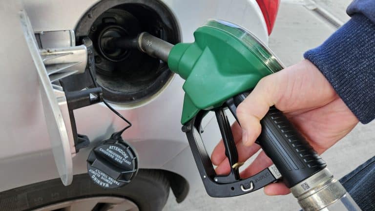 Osoba tankuje paliwo do samochodu na stacji benzynowej, widoczny dystrybutor i pistolet.