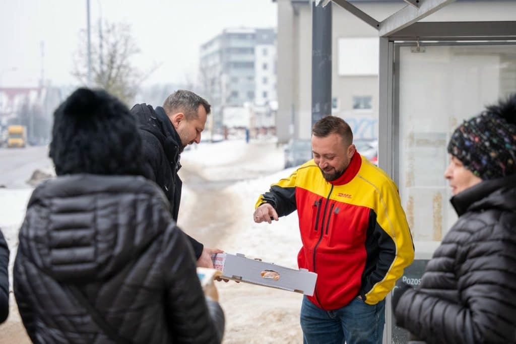 Prezydent Olsztyna rozdaje pączki mieszkańcom na ulicy w zimowej scenerii.