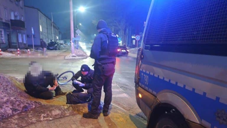 Policjanci udzielają pomocy mężczyźnie z obrażeniami twarzy na jezdni, obok radiow&oacute;z, nocą.