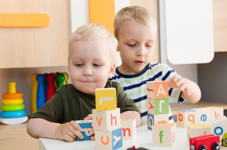 Dwoje dzieci bawi się klockami z literami w przedszkolu, w tle kolorowe zabawki.