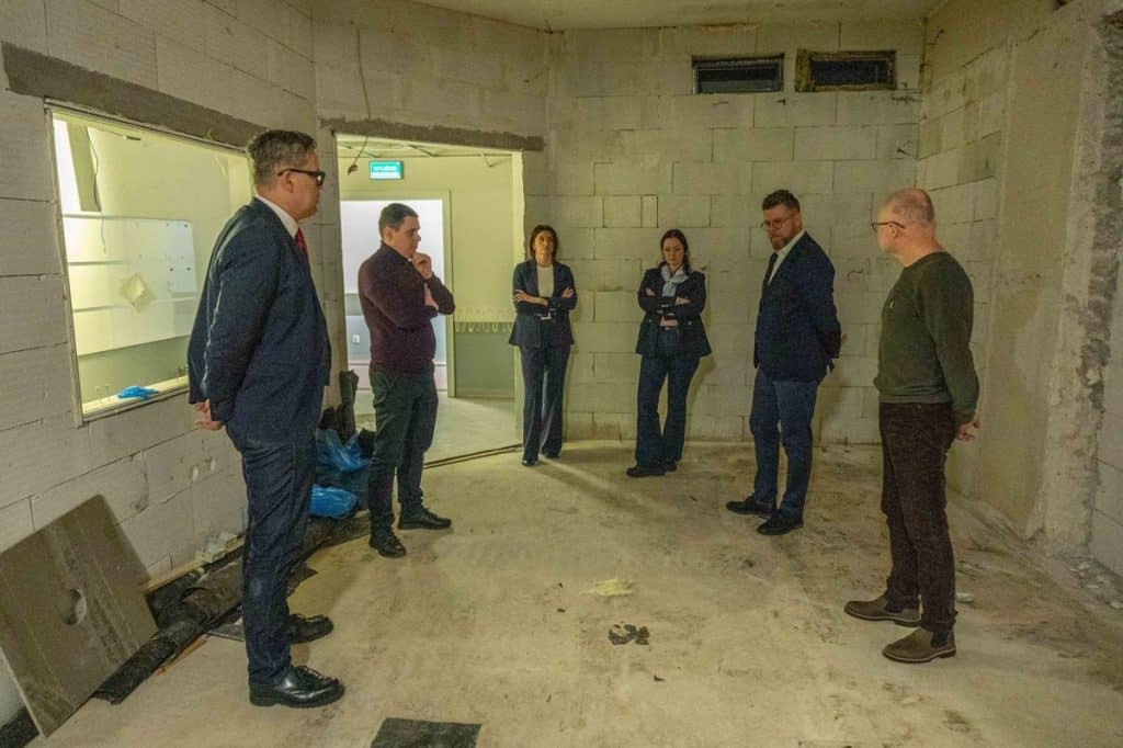 Grupa ludzi w nieukończonym pomieszczeniu szpitalnym, przygotowujących się do instalacji nowoczesnego rezonansu magnetycznego.