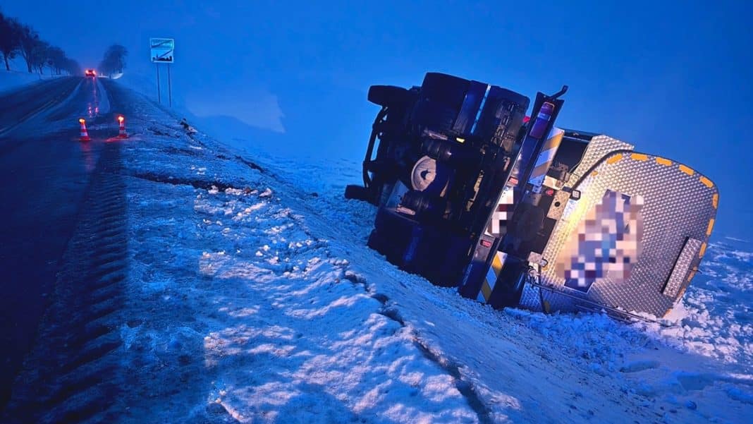 Wywr&oacute;cony ciężar&oacute;wka na poboczu drogi wojew&oacute;dzkiej w zimowych warunkach, widok o zmierzchu.