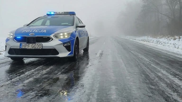 Policja na zaśnieżonej i oblodzonej drodze w mglistym otoczeniu, warunki trudne do jazdy.