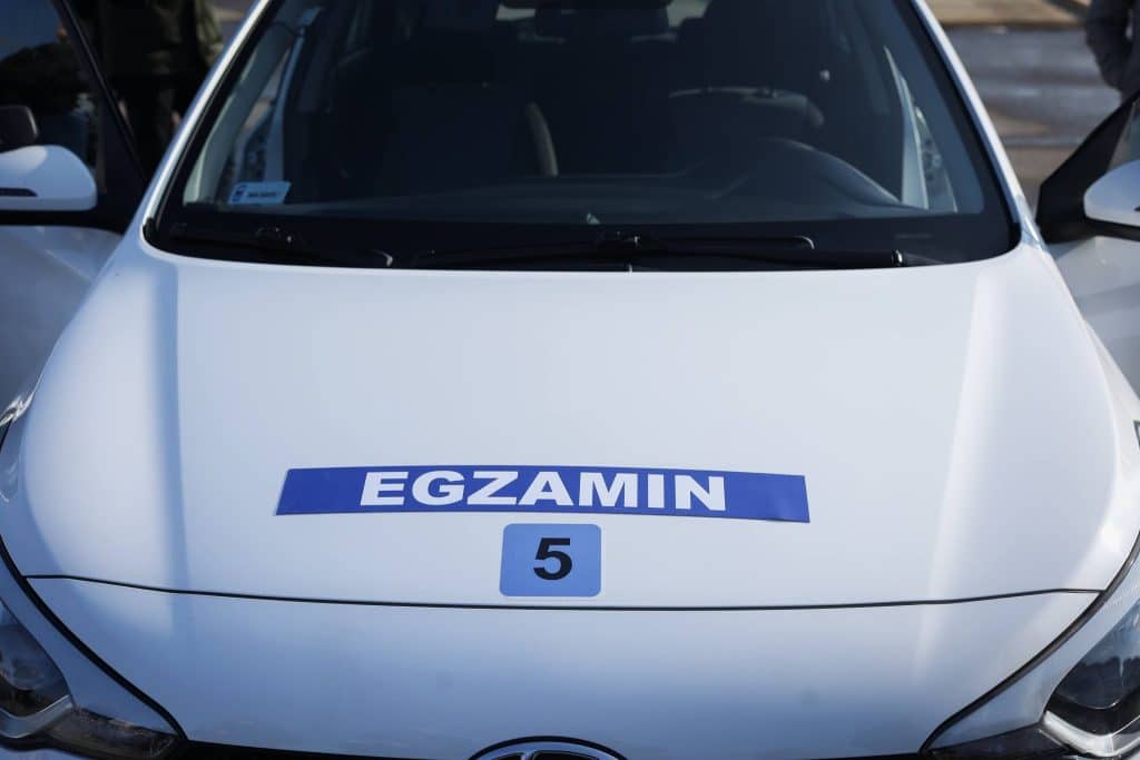 Samoch&oacute;d z naklejką 'EGZAMIN' na przedniej szybie, przygotowany do egzaminu na prawo jazdy.