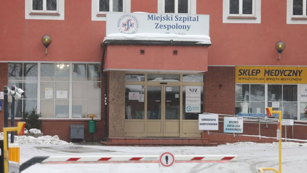 Budynek szpitala z widocznym wejściem i oznaczeniem Miejski Szpital Zespolony w Olsztynie, na zewnątrz śnieg.
