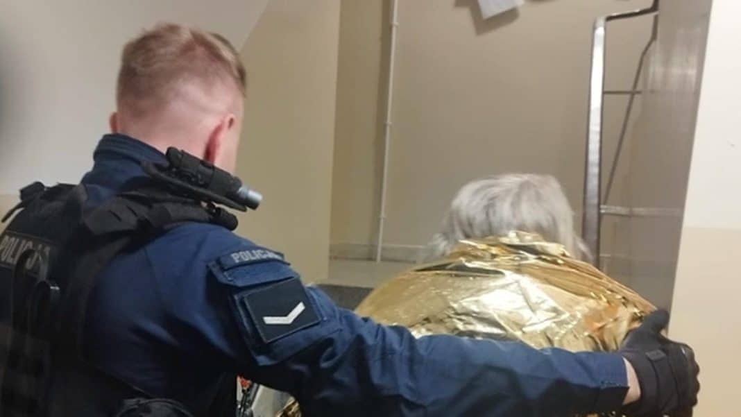 Mężczyzna ubrany w złoty materiał przewraca się przed blokiem na Jarotach w Olsztynie, obok niego policjant.