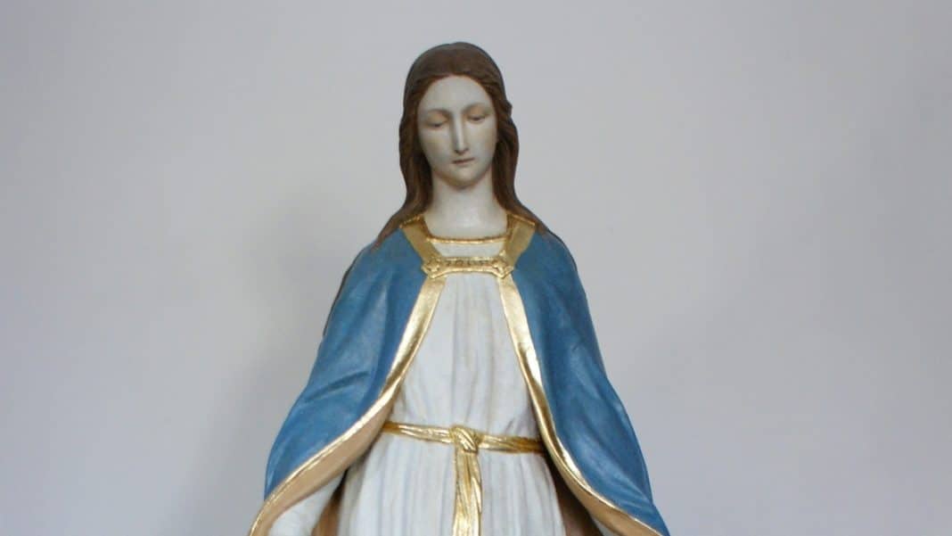 Figura Matki Bożej w Gietrzwałdzie, ubrana w niebieską szatę z złotymi detalami, na jasnym tle.