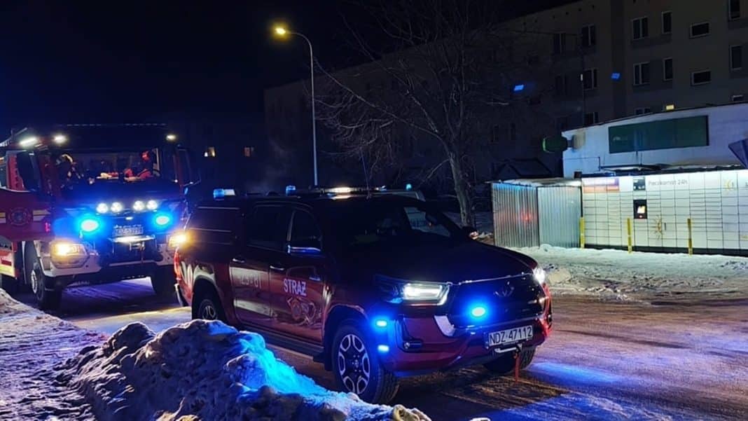 Akcja ratunkowa służb ratunkowych w nocy, w tle pojazdy z włączonymi światłami, zimowa sceneria.