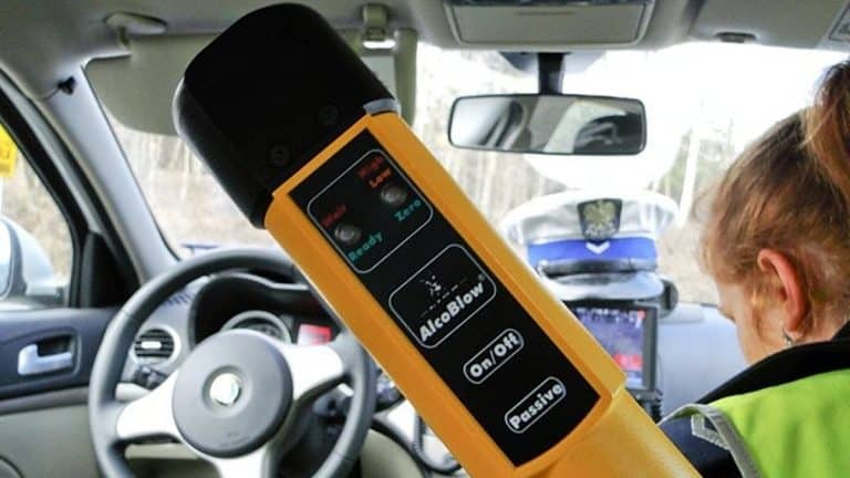 Urządzenie do pomiaru alkoholu w organizmie w samochodzie policyjnym, widoczny radiow&oacute;z i funkcjonariuszka.