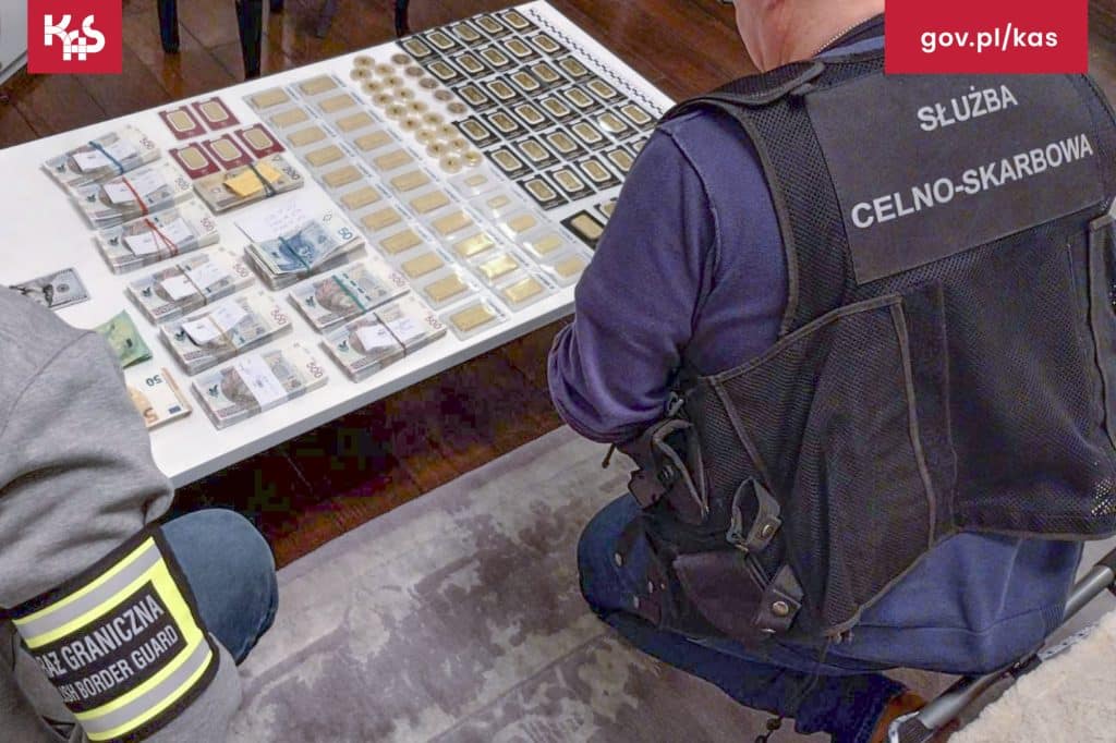 Funkcjonariusz służb celno-skarbowych przy stole z zabezpieczonymi pieniędzmi i innymi przedmiotami.