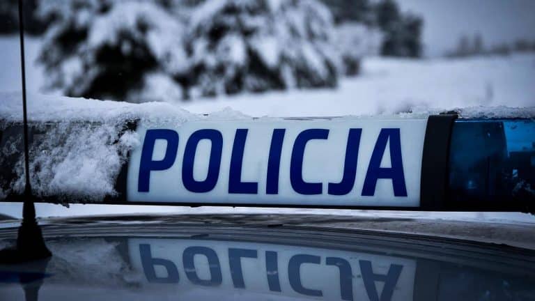 Zdjęcie policyjnego oznakowania na tle zaśnieżonego otoczenia, z napisem 'POLICJA'.