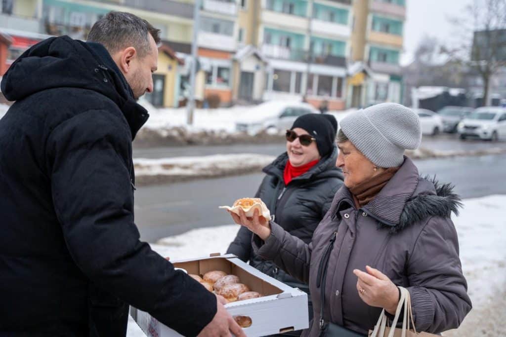Prezydent Szewczyk rozdaje pączki mieszkańcom na ulicy w zimowej scenerii.