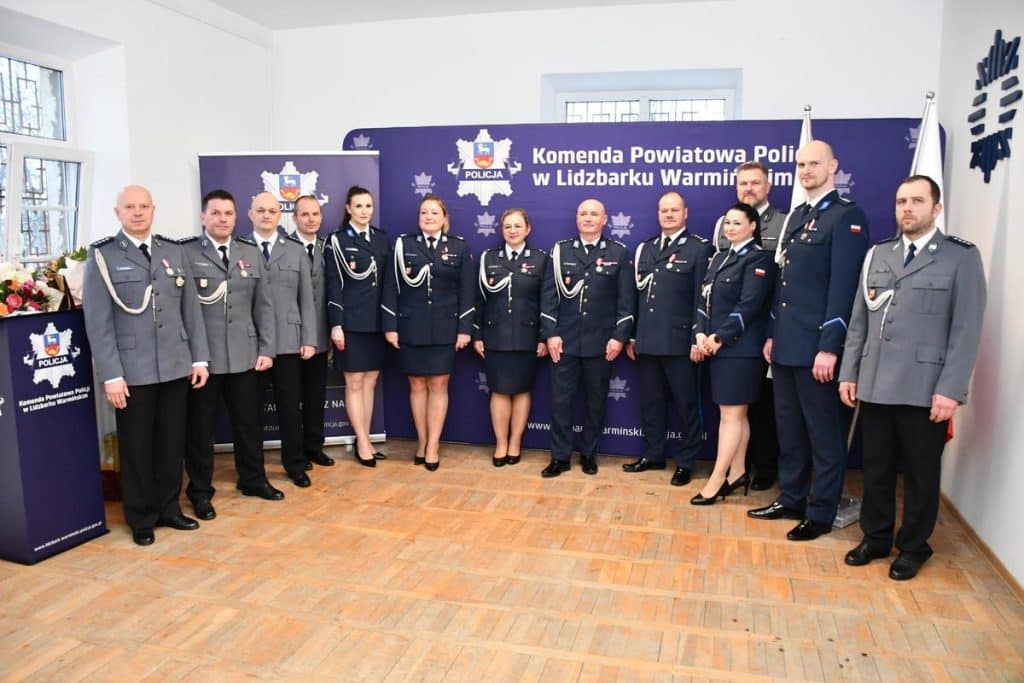 Grupa policjant&oacute;w w uniformach na tle tablicy z napisem o komendzie w Lidzbarku Warmińskim.