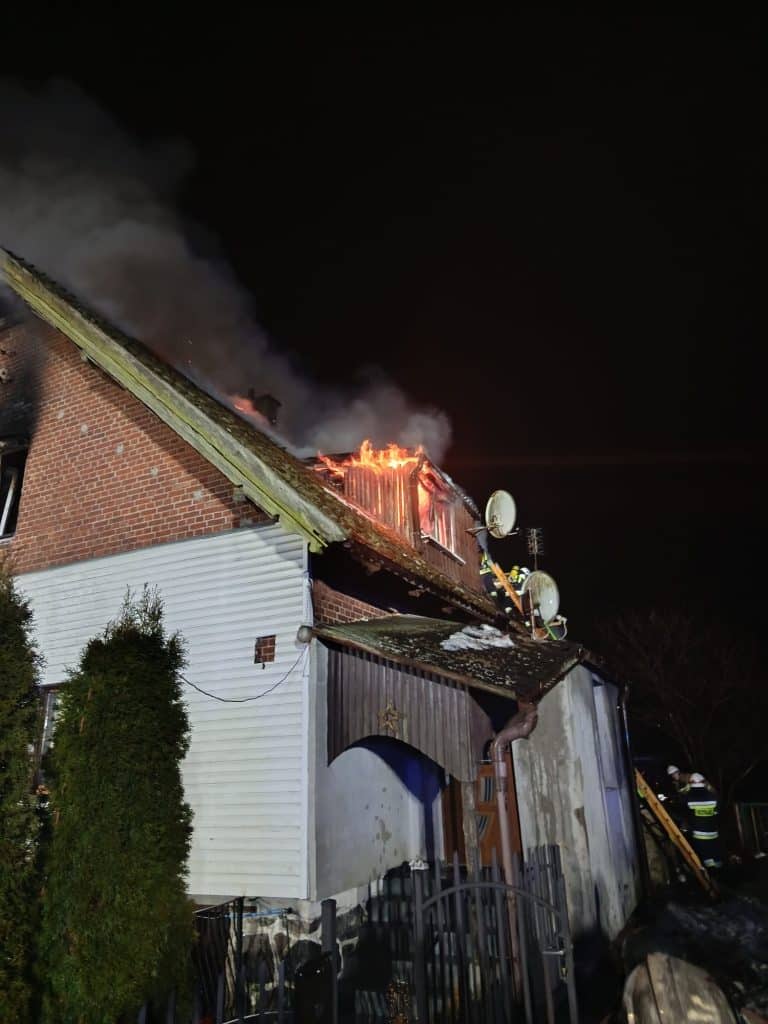 Pożar domu na Mazurach, widoczny ogień i dym nocą, strażacy w akcji.