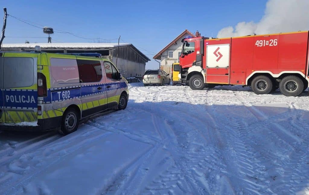 Straż pożarna i policja na miejscu pożaru budynku gospodarczego w Inulcu, w tle obora, na śniegu.