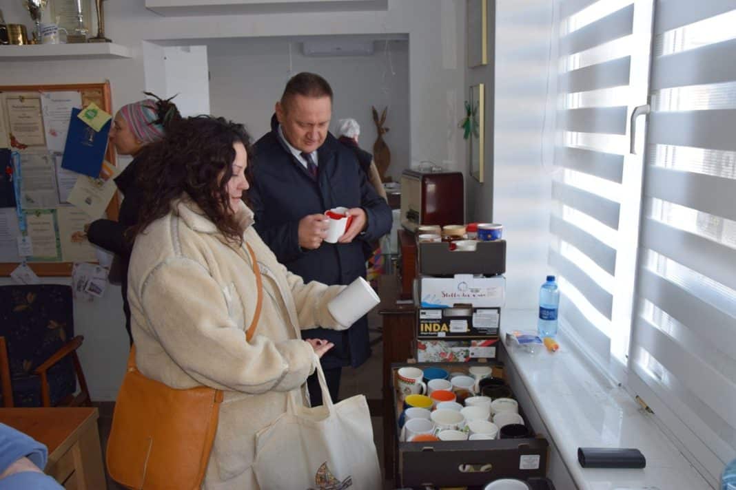 Osoby wybierające kubki z akcji charytatywnej w pomieszczeniu, na stole stoją kubki i pudełka.