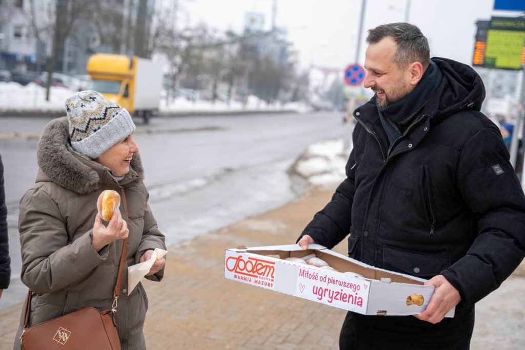 Prezydent Olsztyna rozdaje pączki mieszkańcom na ulicy w zimowej aurze.