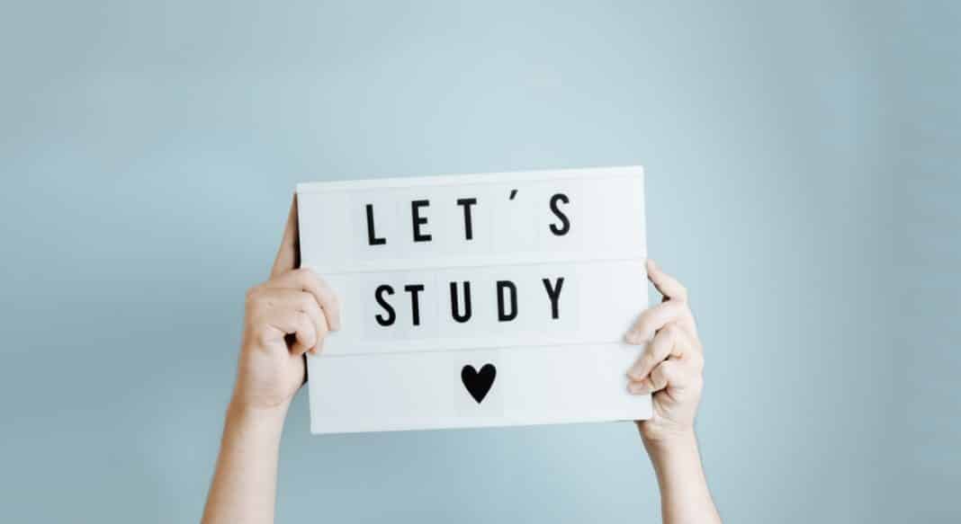 Dłoń trzyma tabliczkę z napisem 'Let's study' na jasnym tle.