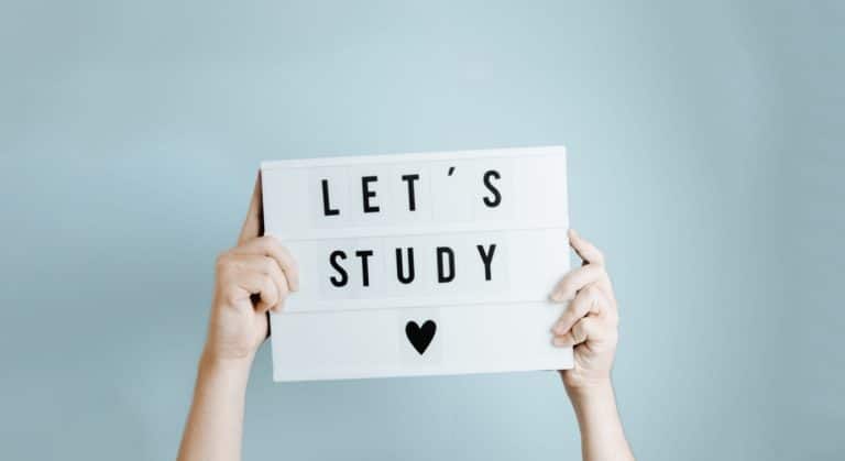 Dłoń trzyma tabliczkę z napisem 'Let's study' na jasnym tle.