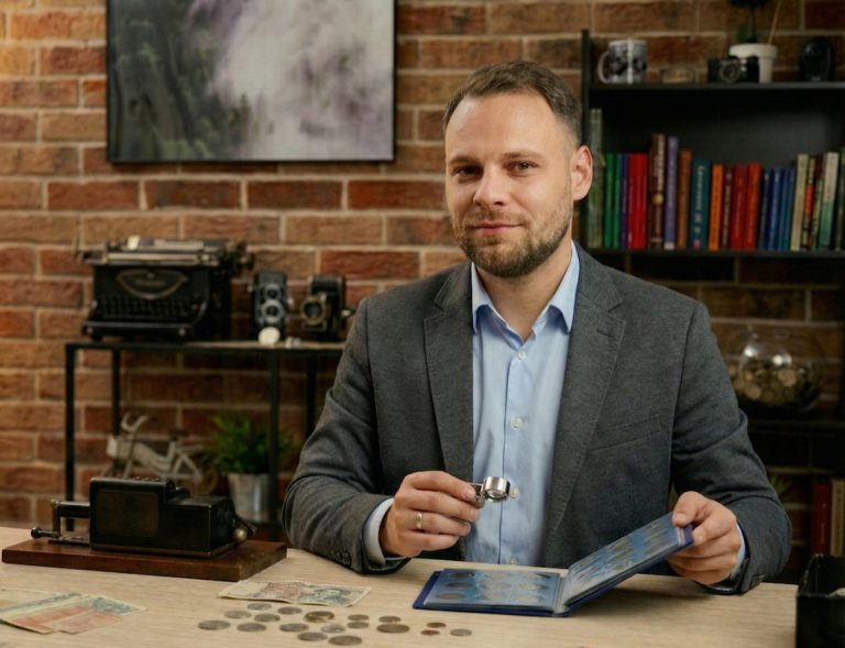 Mężczyzna w biurze z kolekcją monet i książek, trzyma lupę i album z banknotami.