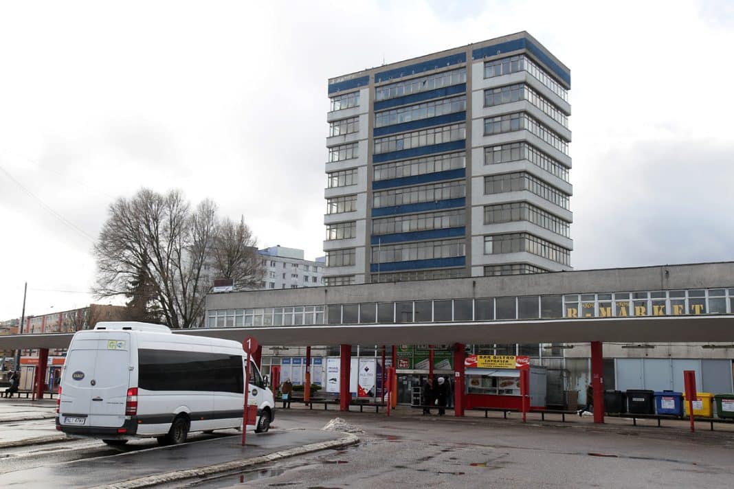 Widok dawnego dworca autobusowego w centrum Olsztyna z autobusem i budynkiem w tle.