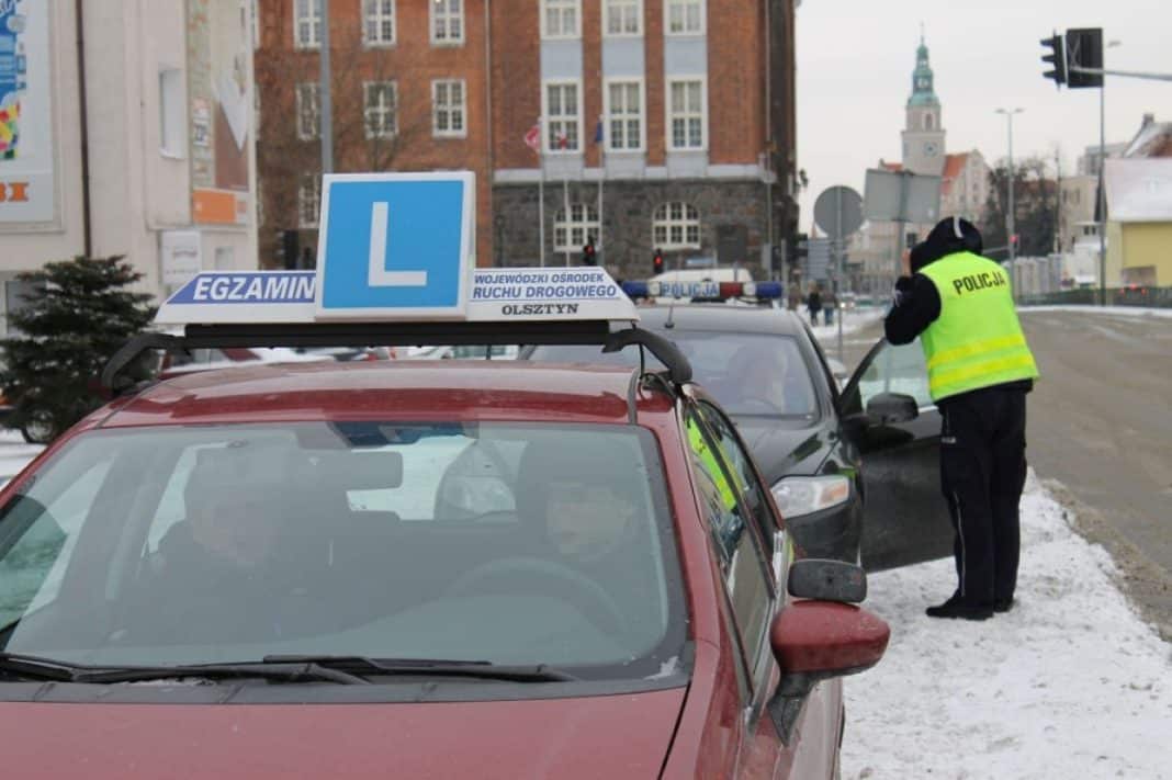 Policjant rozmawia z kierowcą przy samochodzie szkoleniowym na ulicy w Olsztynie zimą.