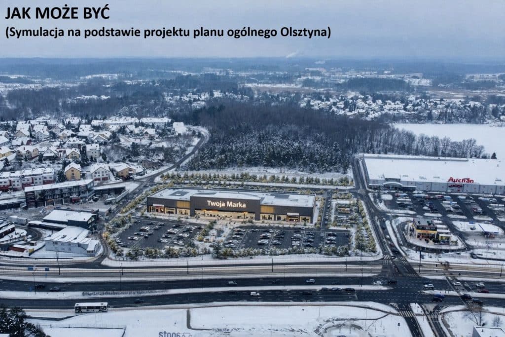 Widok na centrum handlowe Auchan i otaczające tereny pokryte śniegiem, z widokiem na lasy i zabudowania mieszkaniowe w tle.