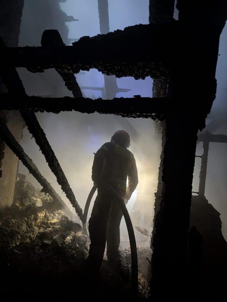 Strażak w akcji podczas gaszenia pożaru domu na Mazurach, widok z wnętrza zniszczonego budynku.