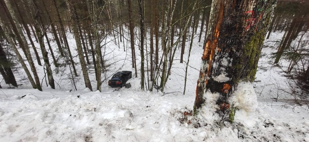 Samoch&oacute;d w lesie po wypadku, wśr&oacute;d drzew i śniegu, zniszczony po uderzeniu w drzewo.
