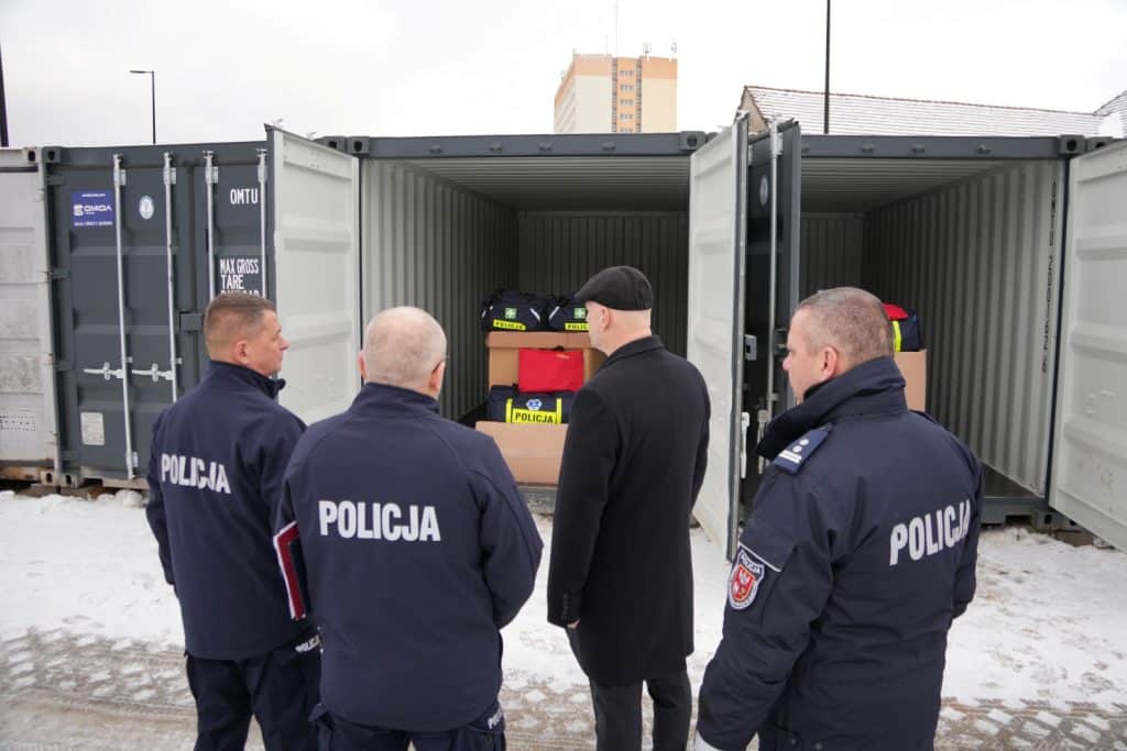 Policjanci przy otwartym kontenerze z wyposażeniem, w tle śnieg i budynki.