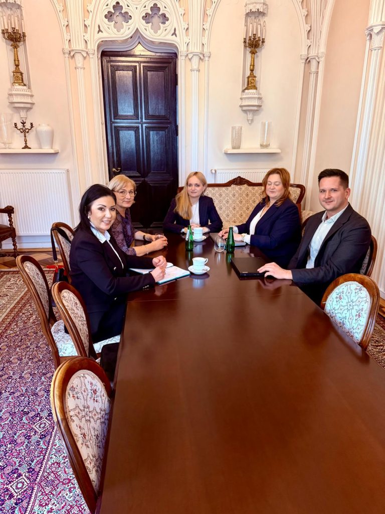 Grupa os&oacute;b podczas spotkania w eleganckim wnętrzu, przy stole z filiżankami i butelkami wody.