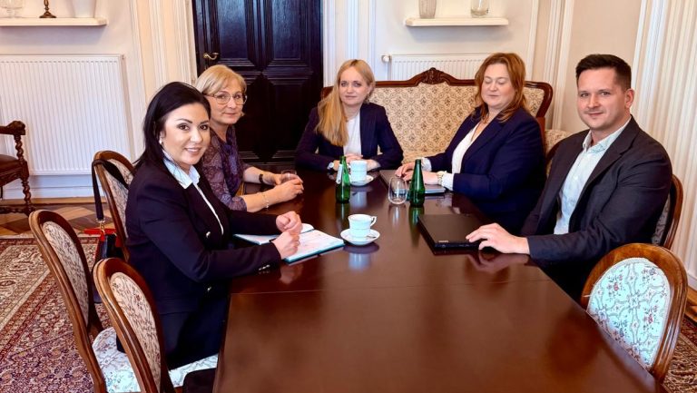 Grupa osób podczas spotkania w eleganckim wnętrzu, przy stole z filiżankami i butelkami wody.