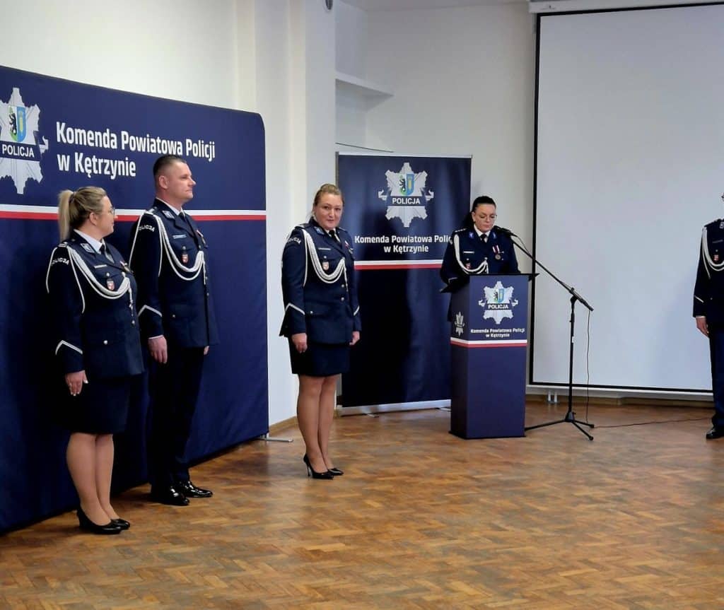 Policjantki i policjanci na konferencji w Kętrzynie, za nimi banery z logo policji.