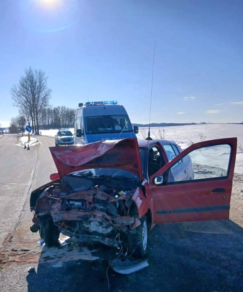 Rozbity samoch&oacute;d na drodze krajowej z wypadniętym z jezdni autem w rowie, w tle policja i zimowy krajobraz.